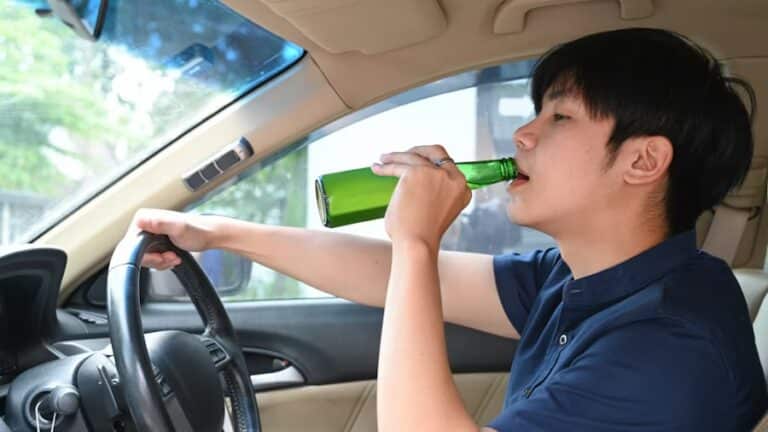 A young man drinking beer while driving a car.