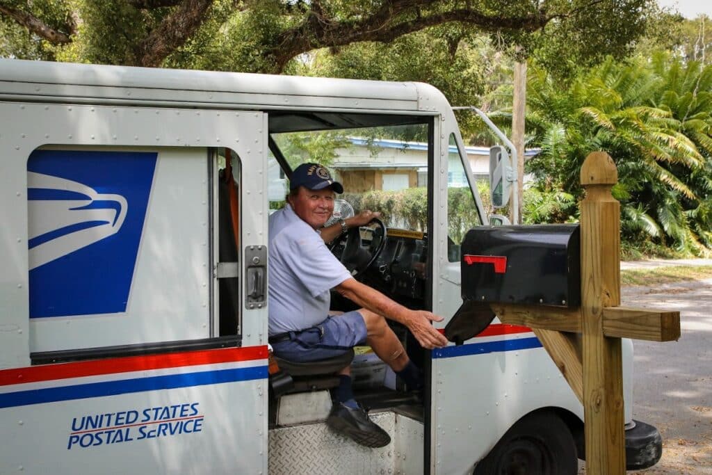 A bus driver in a blue shirt sitting on a white and blue bus during the daytime