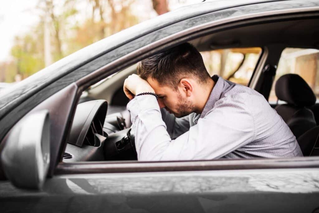 A distressed young man sits in the driver's seat