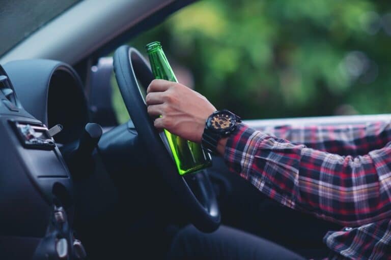 A driver holding a beer bottle while gripping a steering wheel
