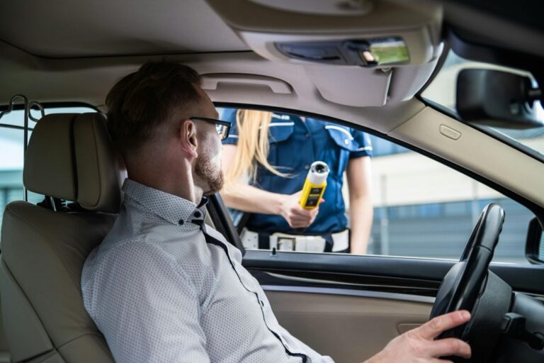A driver seated in a car while a police officer holds a breathalyzer device outside the window