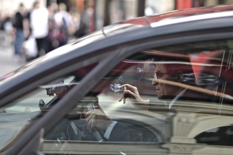 A man in a suit smoking a cigarette while sitting behind the wheel of a car