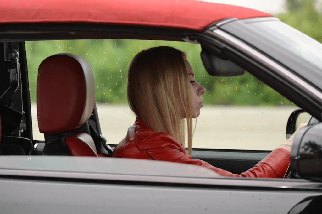 Side profile of a young girl in a red jacket driving a convertible with a red interior