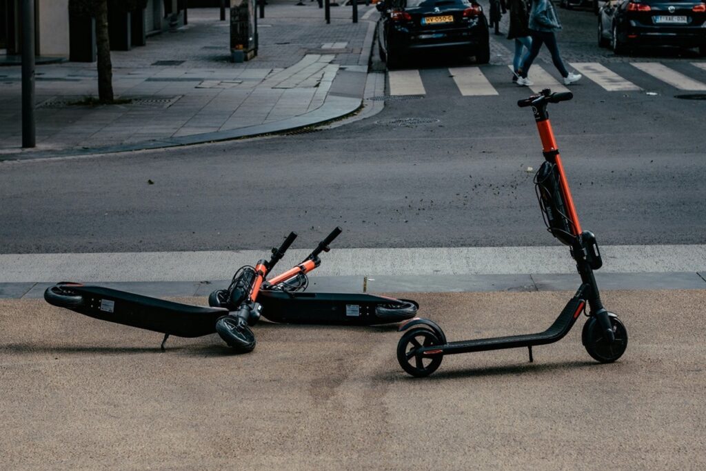 Two electric scooters on a city street, one upright and one lying on its side near a crosswalk intersection