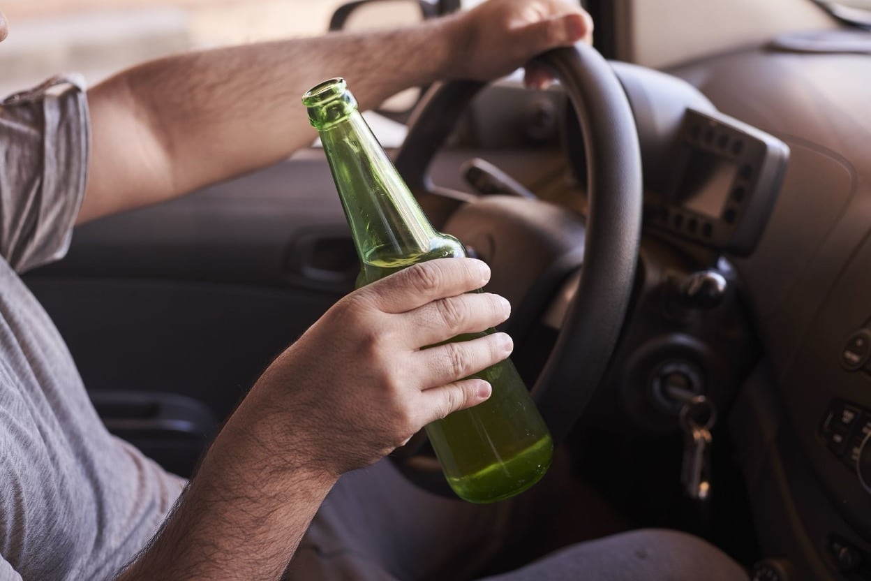 A driver holding a beer bottle with one hand while steering with the other.