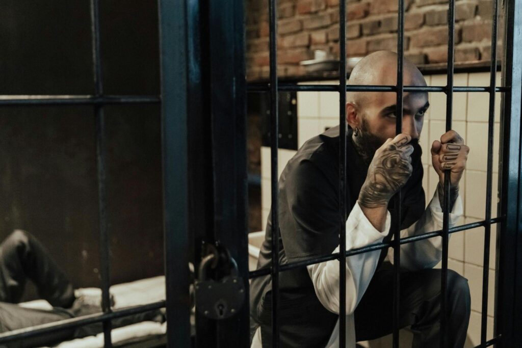 A man gripping jail cell bars, looking out with a serious expression.