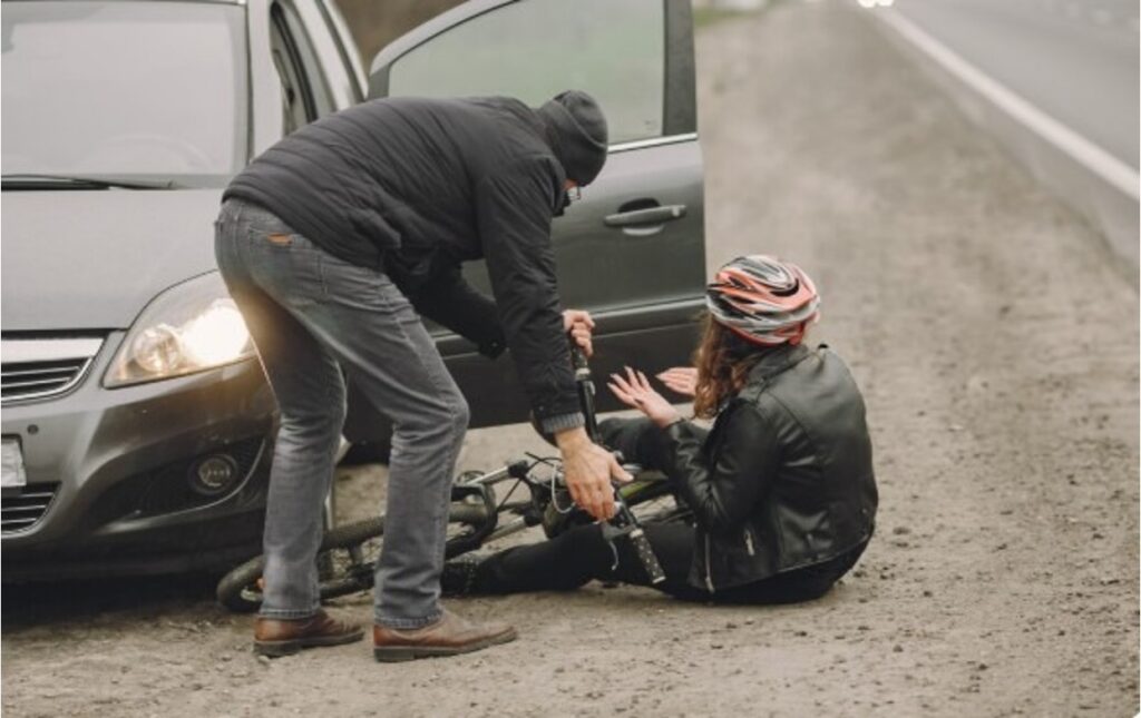 A person on a bicycle falls to the ground beside a car as a driver hits from behind