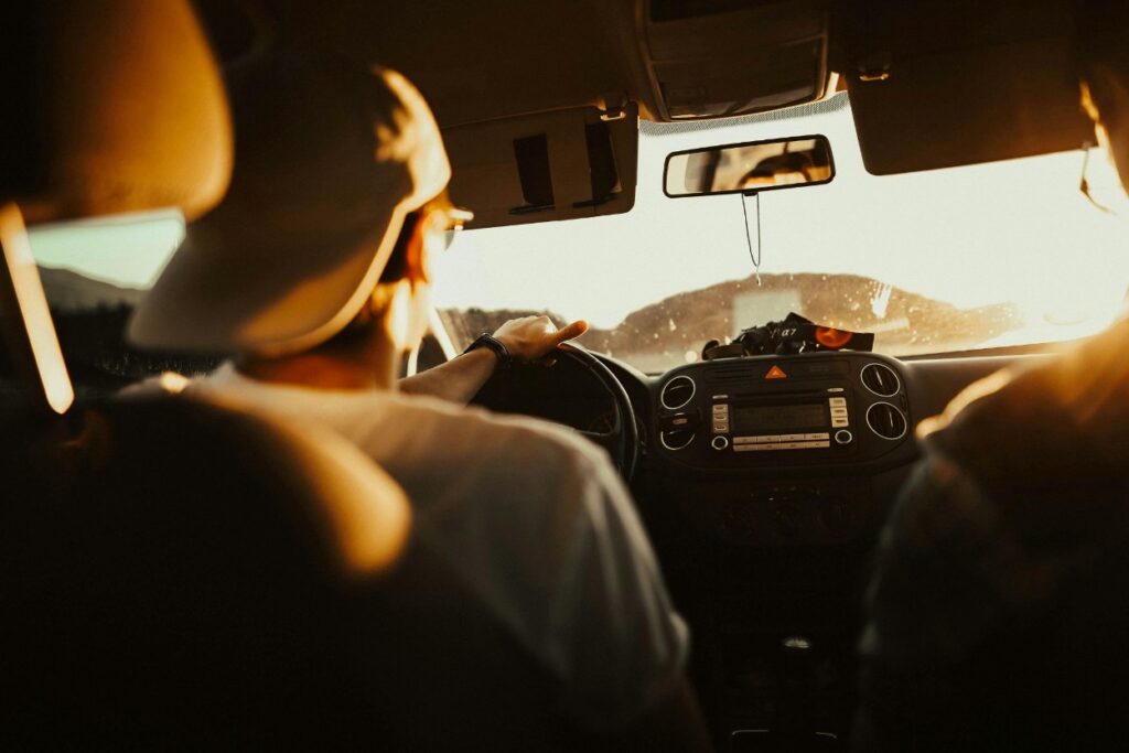 A teenager wearing a hat backward and driving a car at sunset