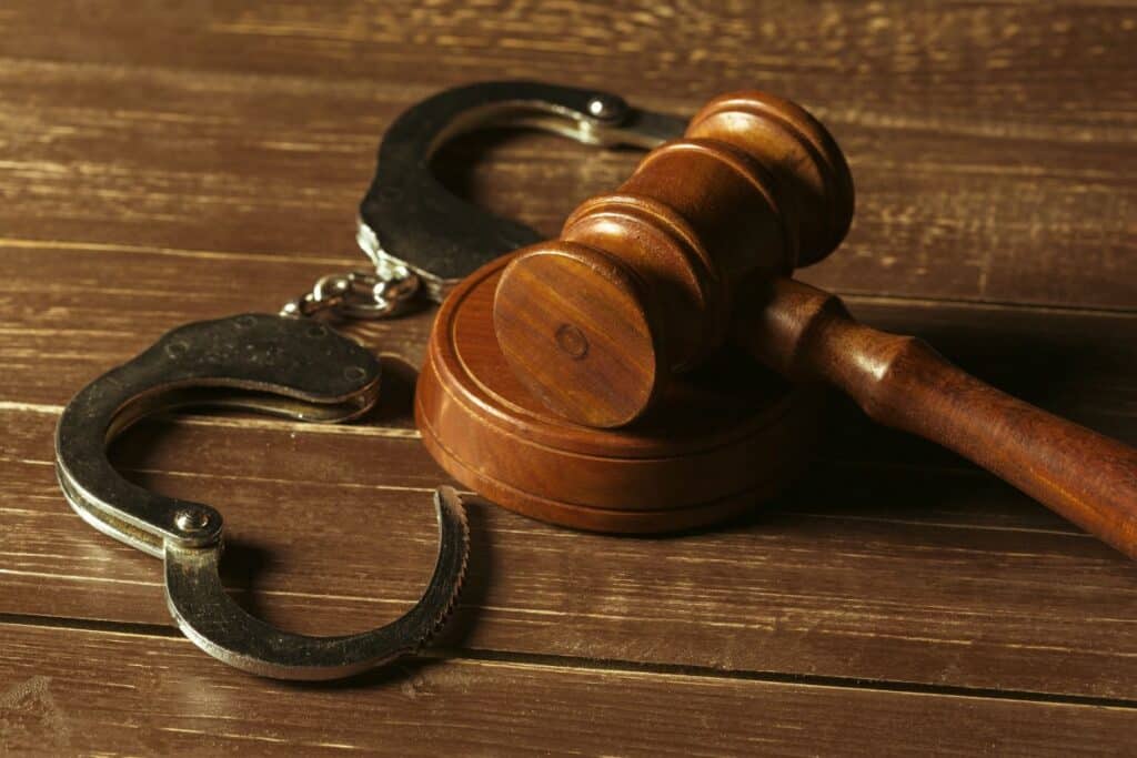A wooden judge's gavel resting beside a pair of open handcuffs on a wooden surface