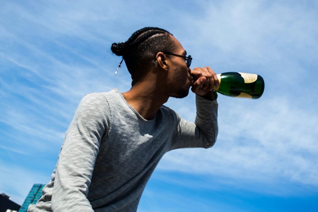 A young man drinks directly from a champagne bottle outdoors