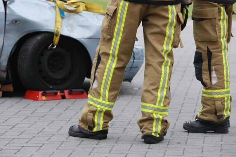 Two firefighters in high-visibility gear standing beside a heavily damaged car